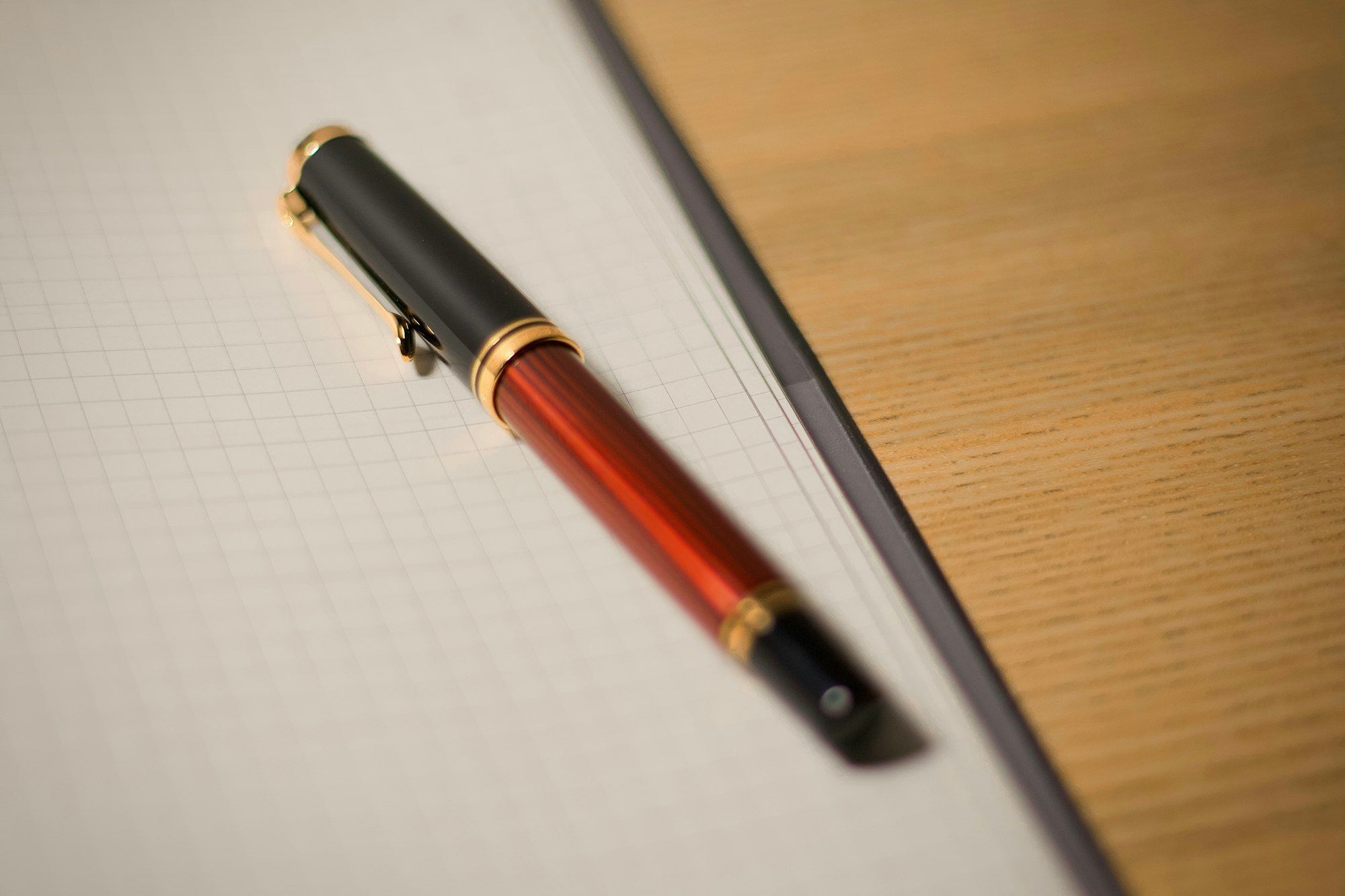 A red and black fountain pen lying on a sheet of squared graph paper on a wooden desk.