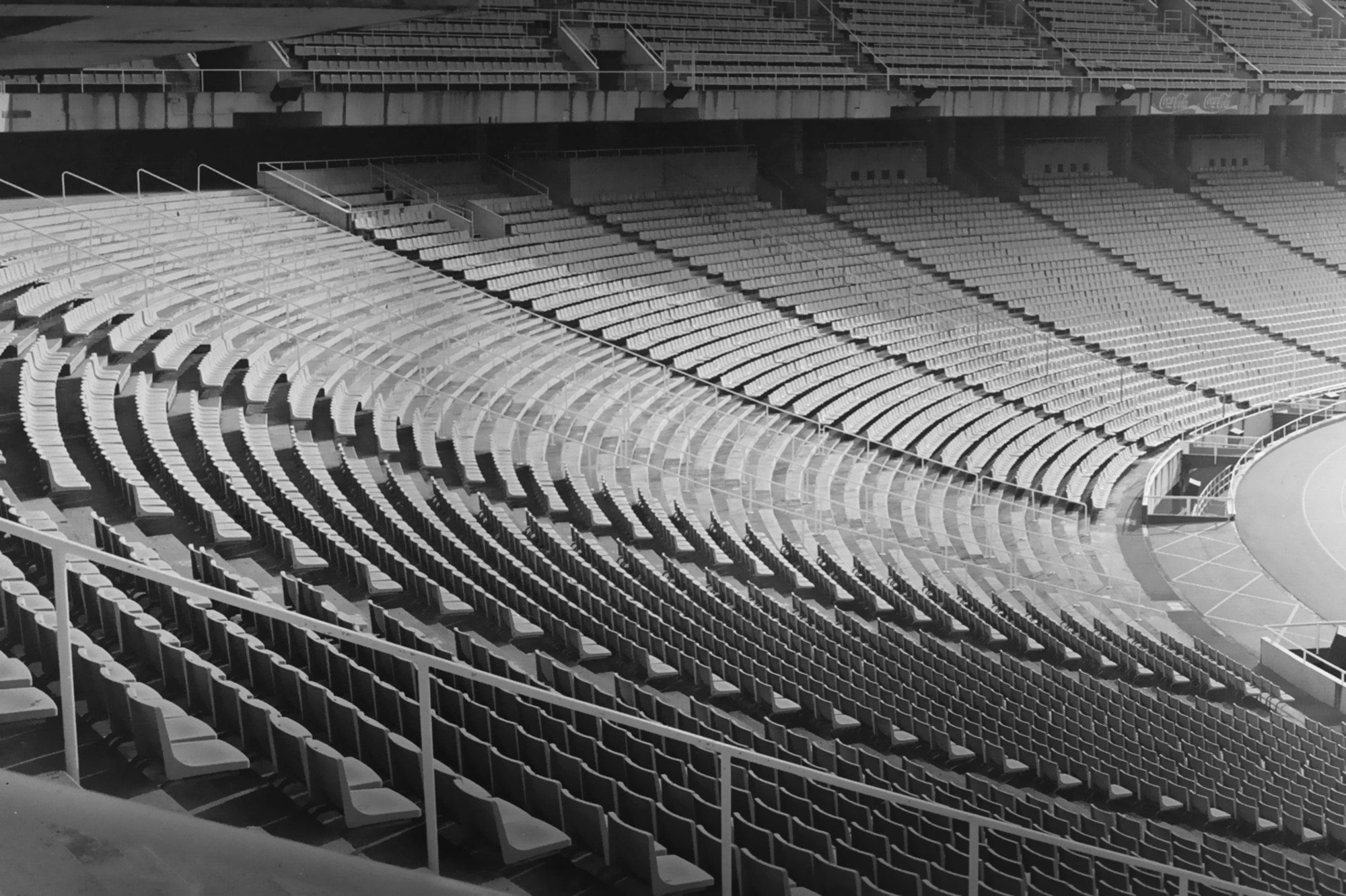 Rows of empty seats curving around an athletics stadium, in black and white.
