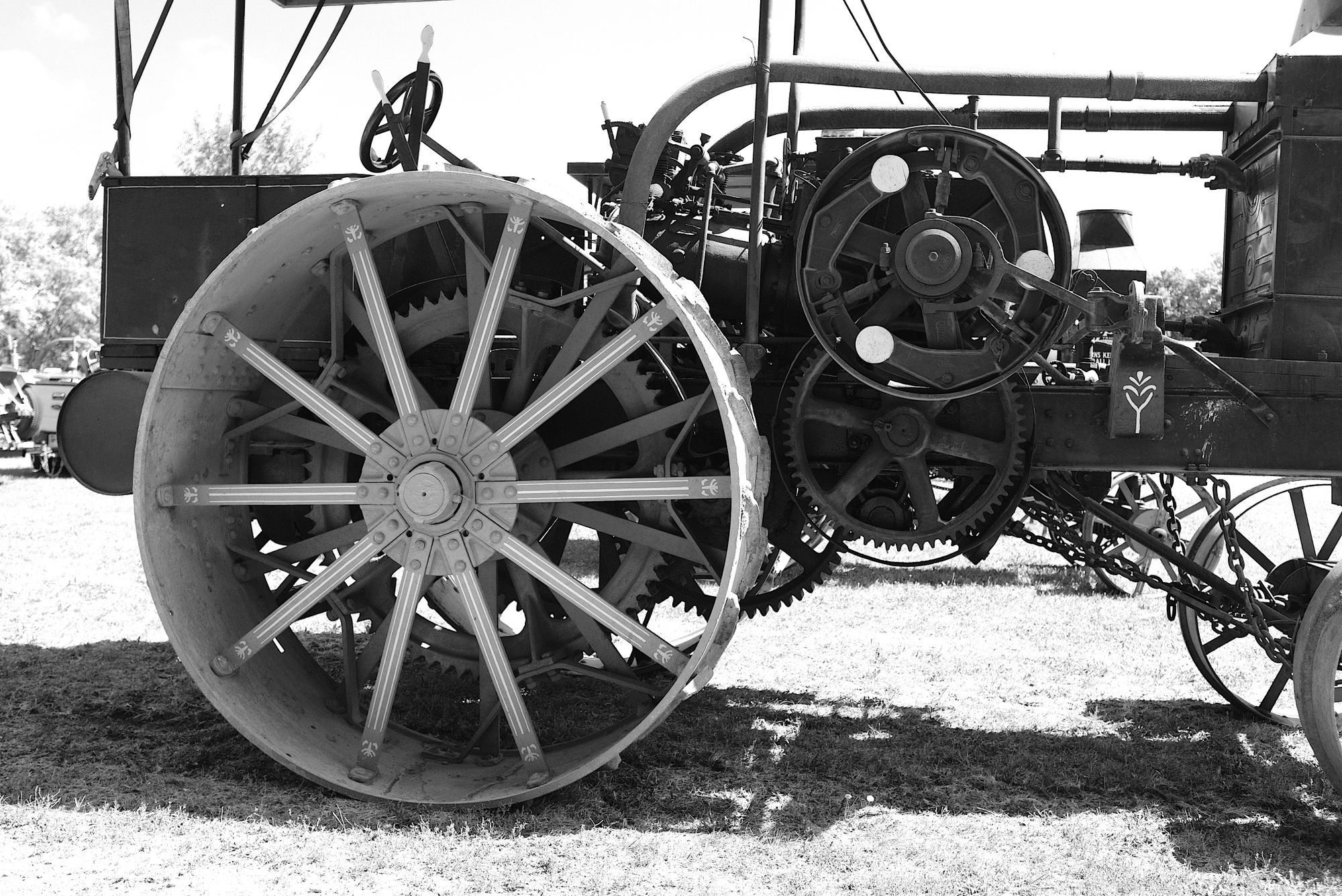 A black-and-white photo of an old steam traction engine, showing its large iron wheel, gears and flywheel.